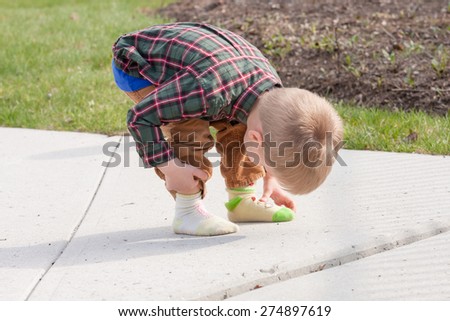 confused toddler dressed in two different socks looking and touching his feet outside on a sidewalk