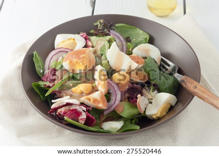 fresh green salad with boiled eggs , red onion and drizzled with balsamic vinaigrette dressing on white background