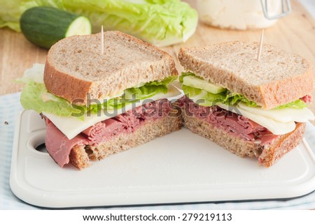 roast beef sandwich with lettuce made with whole wheat bread on white cutting board