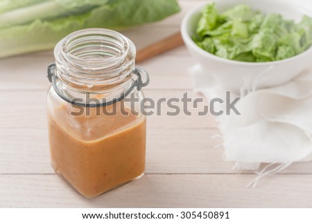 salad dressing with a salad in a glass container on light wooden background