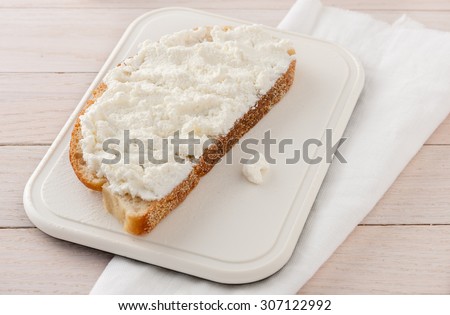 slice of bread with farmer\'s cheese only on white chopping board