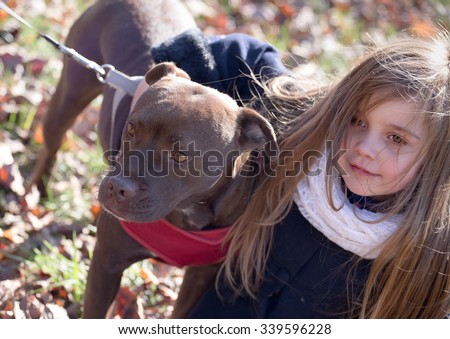 a brown dog on a leash with pink collar being hugged by a little girl on a chilly autumn day, great concept image - children caring for pets