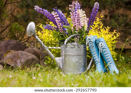 Garden tools. Composition of metallic watering can, rain boots and straw hat.