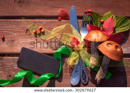 Autumn border from mushrooms, berries, cutlery and fallen leaves on old wooden table. Thanksgiving day concept. Background with tag/ sticker/ with copy space for your text. Happy Thanksgiving day.