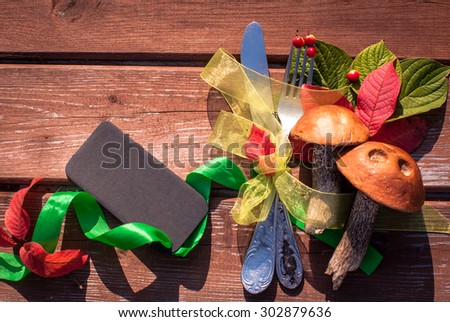 Autumn border from mushrooms, berries, cutlery and fallen leaves on old wooden table. Thanksgiving day concept. Background with tag/ sticker/ with copy space for your text. Happy Thanksgiving day.