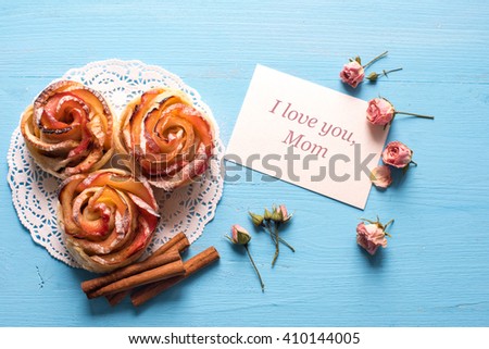 Homemade Apple rose cake with sugar powder on blue  wooden background.\
Top view.  Handmade gift for mom/ Mothers day concept card.