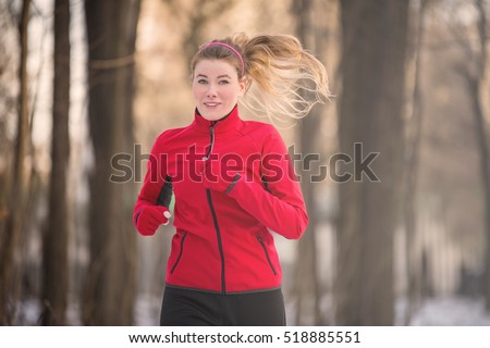 Winter running exercise. Runner jogging in snow. Young woman fitness model running in a city park