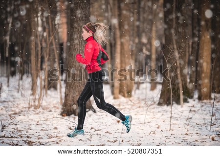 Winter running exercise. Runner jogging in snow. Young woman fitness model running in a city park