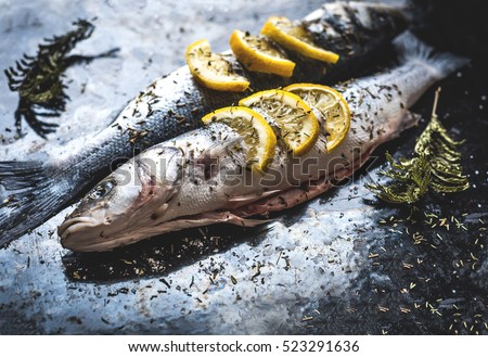 Fish dish cooking with various ingredients. Raw Sea bass with lemon, garlic, herbs and spices on cutting board, top view. Healthy food or diet nutrition concept.