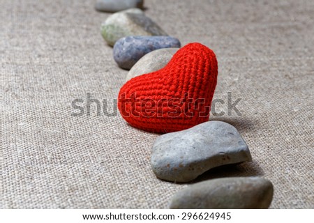 Red heart in row of stones on textile background. Shallow focus on heart.