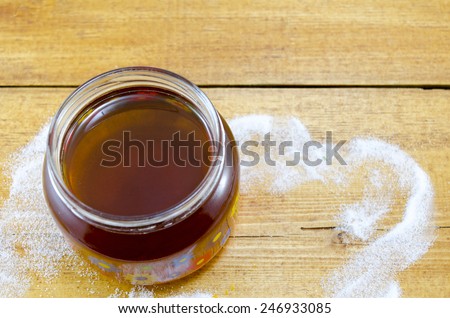 Jar of dark honey on a table decorated with sugar
