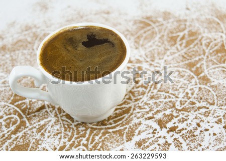 Cup of coffee on a white table covered with grounded coffee