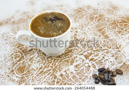 Cup of coffee on a white table covered with grounded coffee