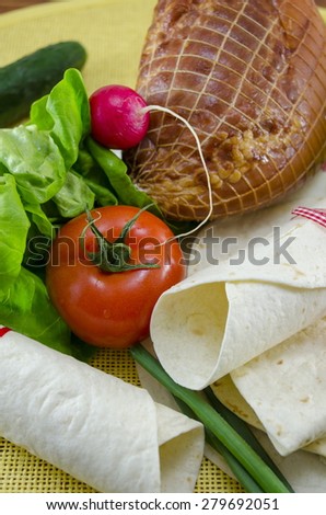 Empty tortillas tied with a red ribbon on a table with tomato, lettuce and ham