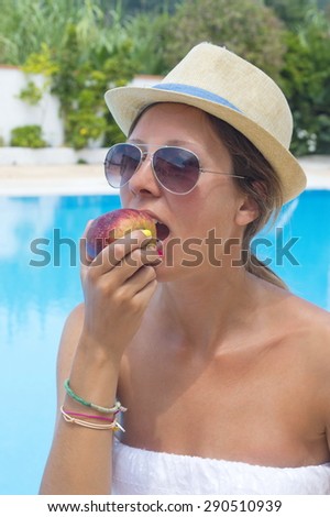 Young girl in bikini eating apple by the pool