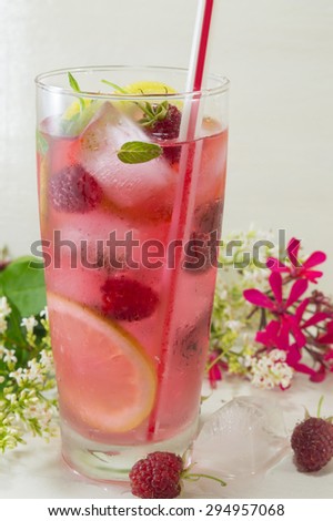 Homemade raspberry ice tea with lemon raspberry and ice cubes on a table decorated with flowers