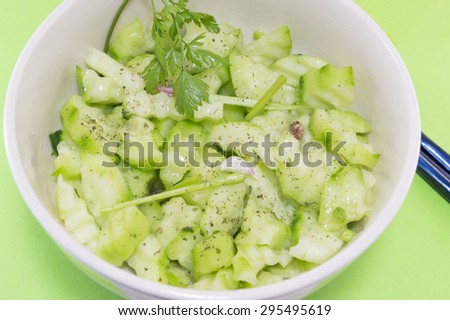 Salad with cucumber and marrow squash with parsley onion next to japanese chopsticks on a green background served