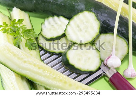 Sliced cucamber and marrow squash  ordered on top of the chopper on a green background