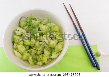 Salad with cucamber and marrow squash with parsley onion next to japanese chopsticks on a green background served