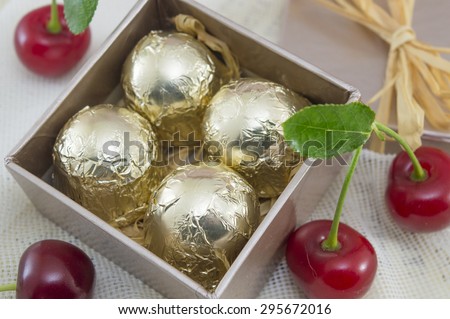 Chocolate candies wrapped in golden coloured packaging in a red present box with fresh cherries