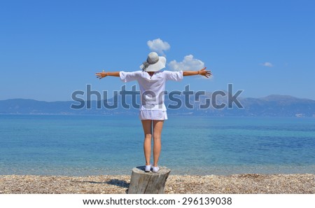 Young woman looking at the mountains above sea with her arms wide open on a sunny summer day
