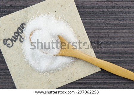 Pile of sugar and a wooden spoon full of sugar on the wooden table