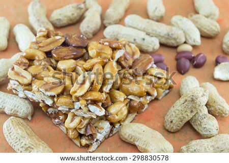 Honey bar with peanuts almonds and hazelnuts surrounded by bunch of roasted and raw peanuts on orange background