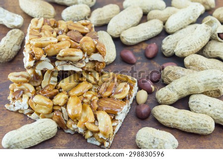 Honey bar with peanuts almonds and hazelnuts surrounded by bunch of roasted and raw peanuts placed on a wooden board