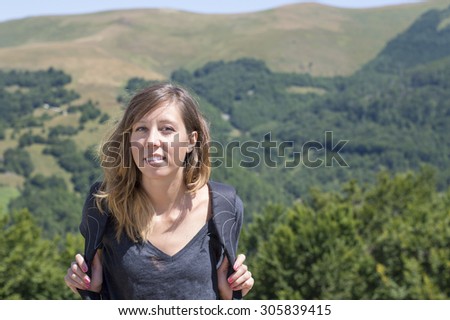 Portrait of happy girl hiker with backpack in the mountains surrounded by green vegetation. Hiking trip