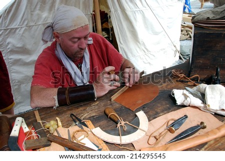 LJUBLJANA, SLOVENIA - AUGUST 24, 2014: Leather dresser (member of historical society Legio I Italica) with ancient tools works in a Roman military camp at celebration of 2000th anniversary of Emona.