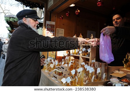 LJUBLJANA, SLOVENIA - DEC. 13, 2014: Customer pays cash for a chosen bottle of honey brandy at kiosk at Christmas and New Year\'s market in open air on the street at pedestrian zone.