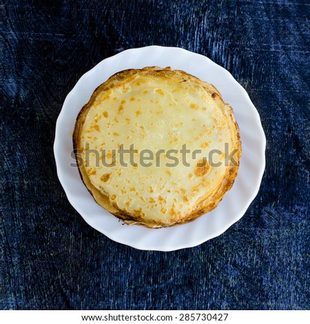Traditional Russian Pancakes on Dark Wooden Background. Delicious breakfast meal. Top View of White Plate with Fresh Baked Homemade Pancakes.