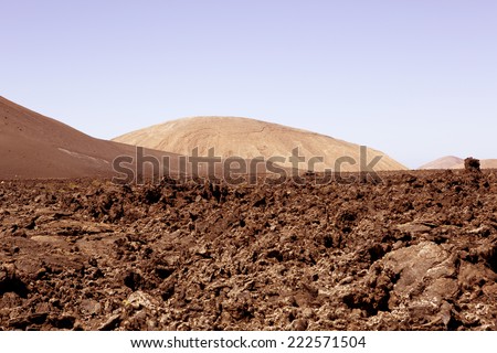 An arid desert or volcanic landscape. Possibly another planet