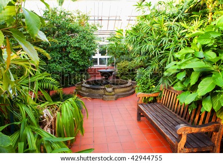 The inside of a Victorian Palm house with bench, fountain and foliage