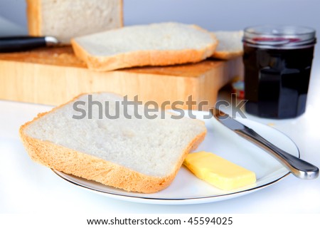 A slice of freshly baked bread on a plate with butter, jam or jelly in the background