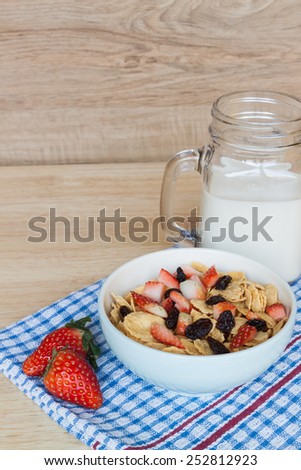 Corn flakes in a bowl with strawberry , Raisins and milk  on wood background