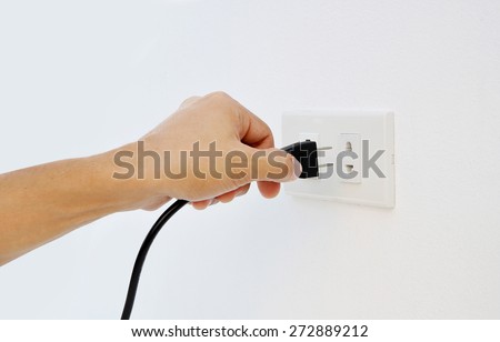 Hand Putting Plug Into Electricity Socket on clean cement plaster wall background