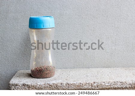 fish pellet in plastic flask with blue cover and space still life on brick block and concrete background