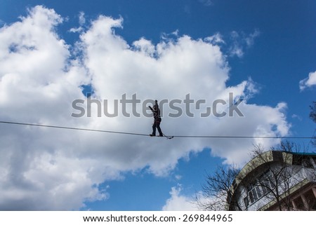 Fearless highliner walking on tight rope over the river on vibrant blue sky background