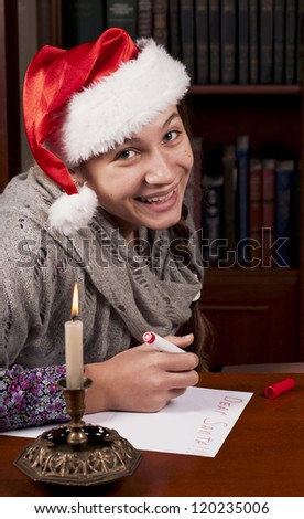 Funny girl in Santa hat writes letter to Santa near christmas tree