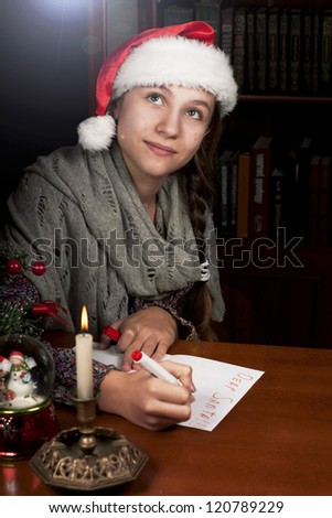 Funny girl in Santa hat writes letter to Santa near cristmas tree