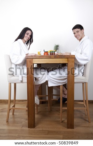 Nice young couple in the morning eating their breakfast in their home, wearing white towel robe.