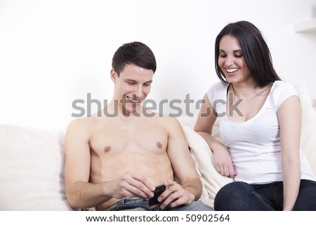 Nice beautiful couple with mobile phone, smiling, relaxing on the white sofa