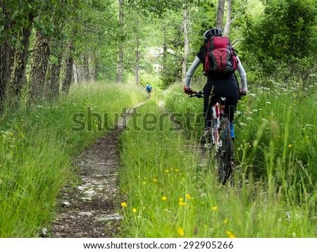Woman riding mountain bike on a dirt road in the forest.