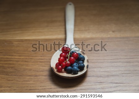 Currants and blueberries on a wooden spoon - focus on the blueberries on the foreground