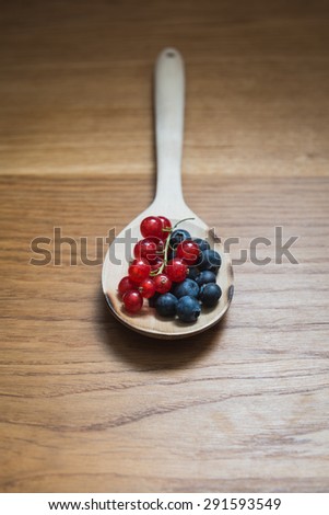 Blueberries and currants on a wooden spoon - focus on the blueberries on the foreground
