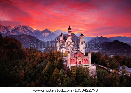 Neuschwanstein fairy tale castle. Beautiful sunset view of the bloody clouds with autumn colours in trees, twilight night, Bavarian Alps, Bavaria, Germany. Travel Europe. Red sky evening with castle.