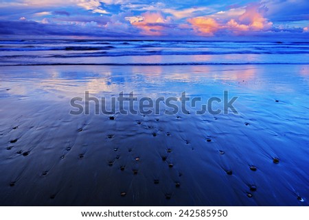 The pebble and sand beach at sunrise, with dark blue wave and orange clouds, Costa Rica coast