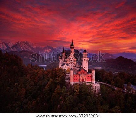 Beautiful early morning view of the Neuschwanstein fairy tale castle, bloody dark sky with autumn colours in the trees during sunrise, twilight, end of night, Bavarian Alps, Bavaria, Germany