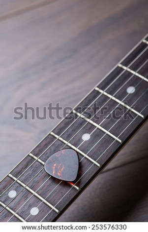 Guitar frets with strings and mediator on dark brown surface